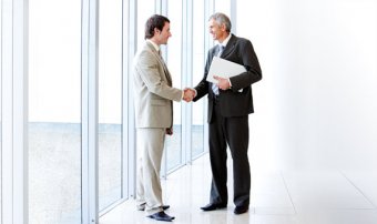 two business men shaking hands next to an office window